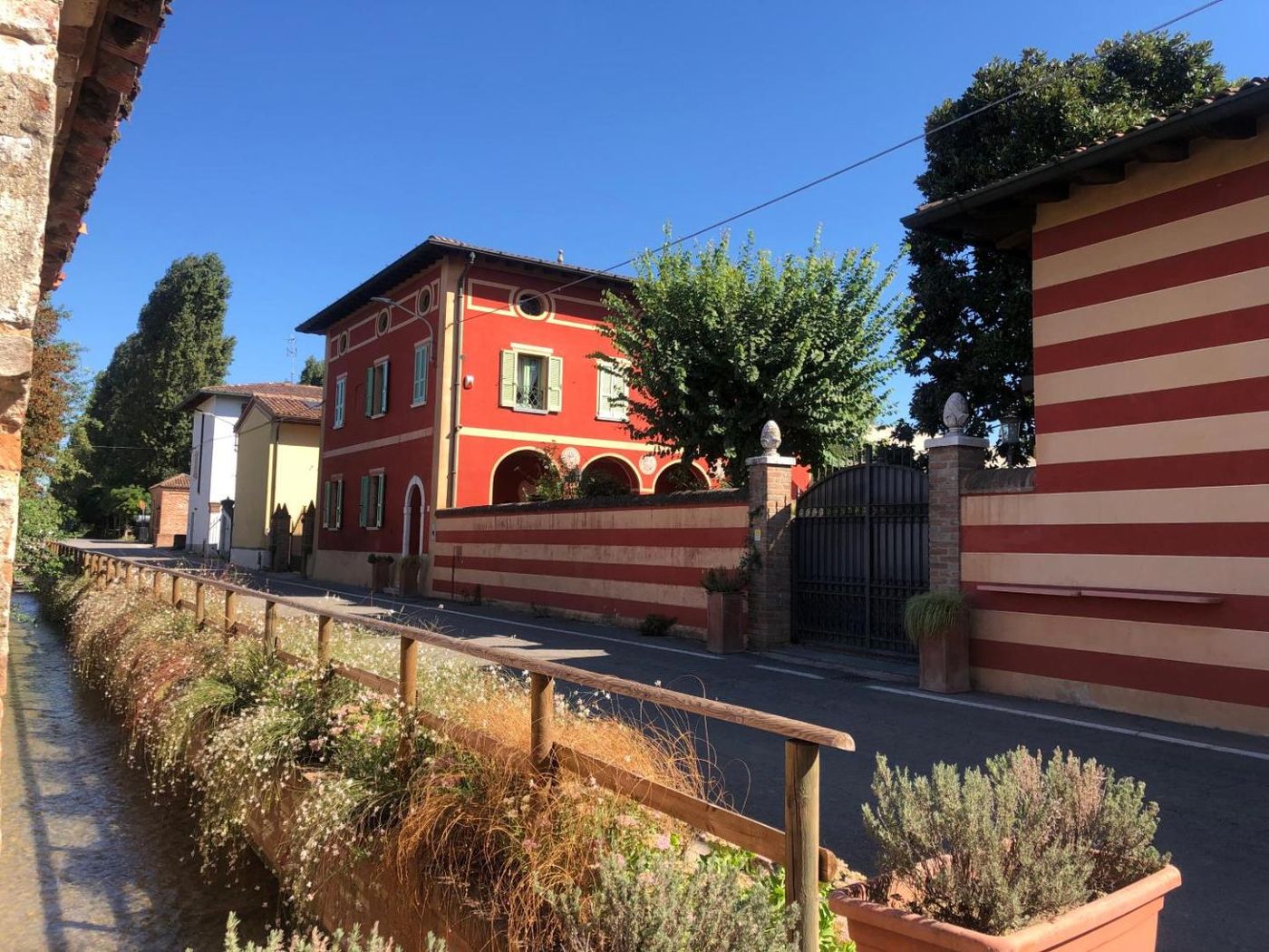 La facciata rossa di Villa La Canonica lungo la roggia del borgo di Padernello